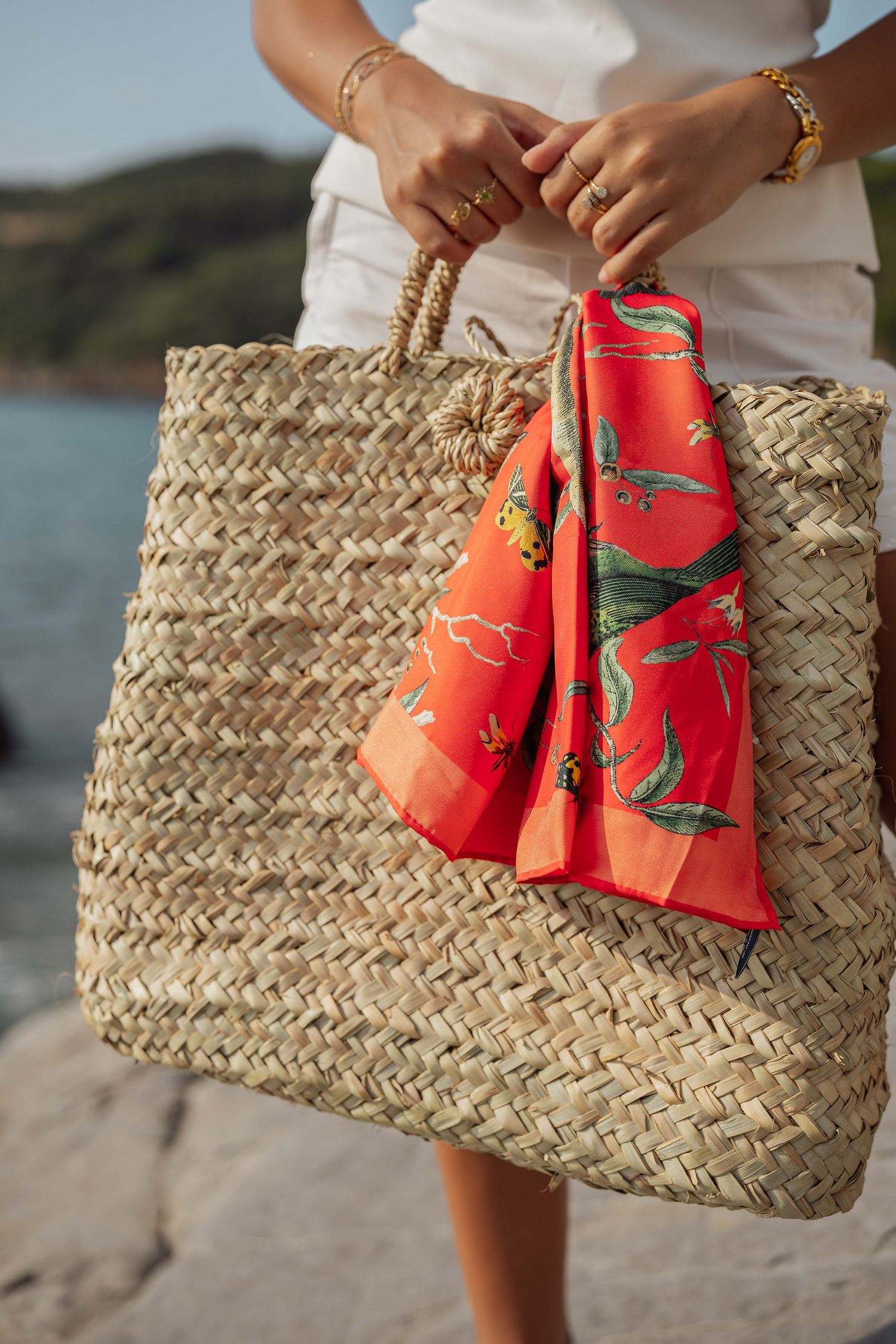 Donna con borsa in paglia naturale Marika Selection indossata su scogli vista mare, accessorio estivo elegante e minimal.