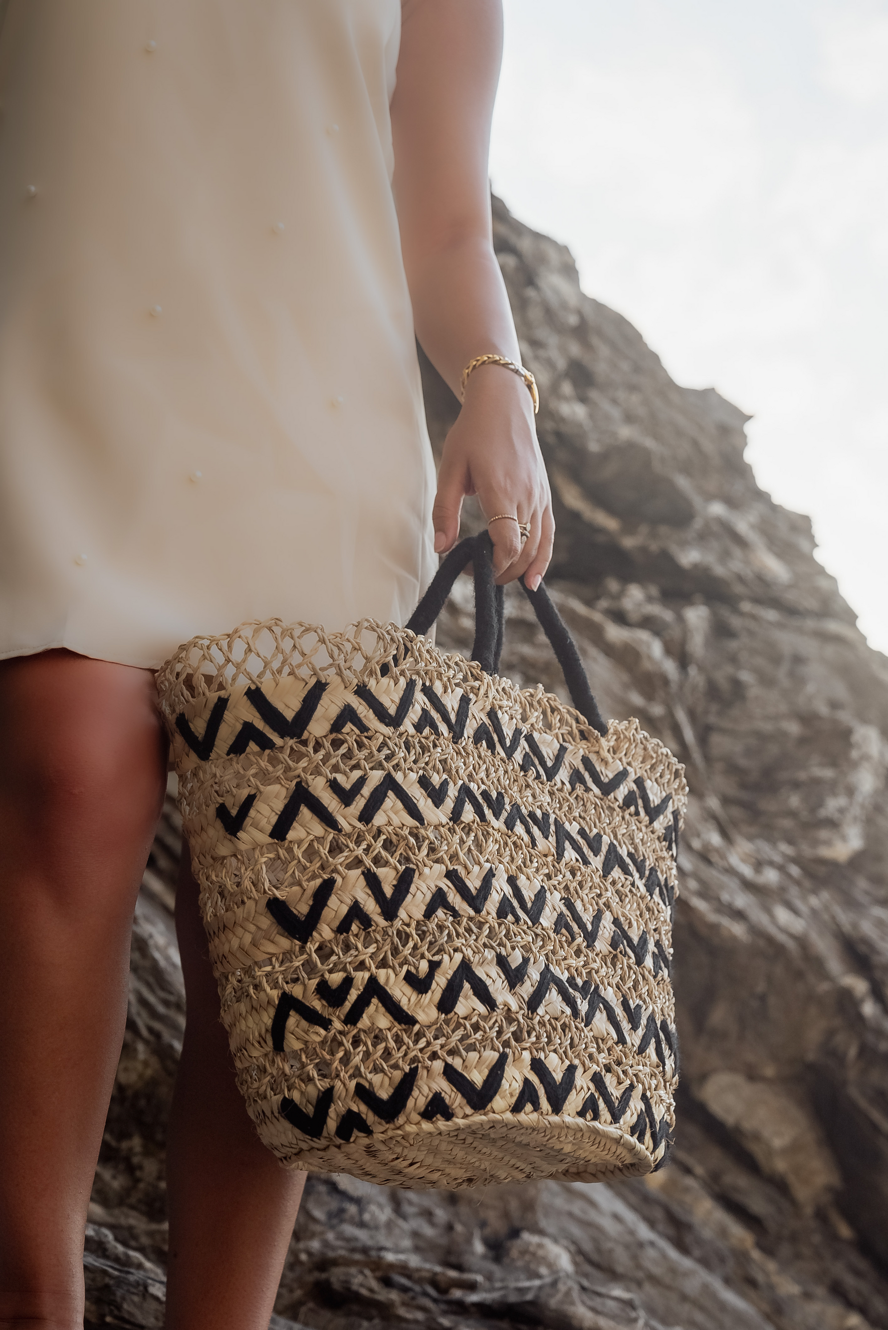 Borsa in paglia naturale intrecciata con motivo geometrico nero, indossata al mare, stile estivo contemporaneo