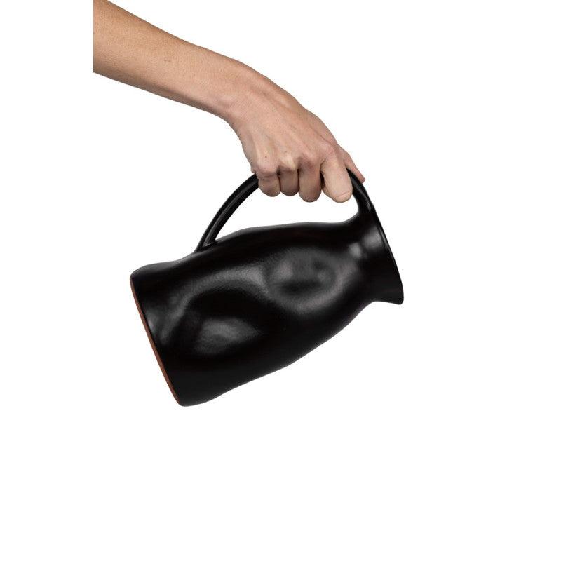 Mano che versa  da una caraffa nera n ceramica smaltata Dutch Deluxes, eleganza artigianale in un gesto quotidiano