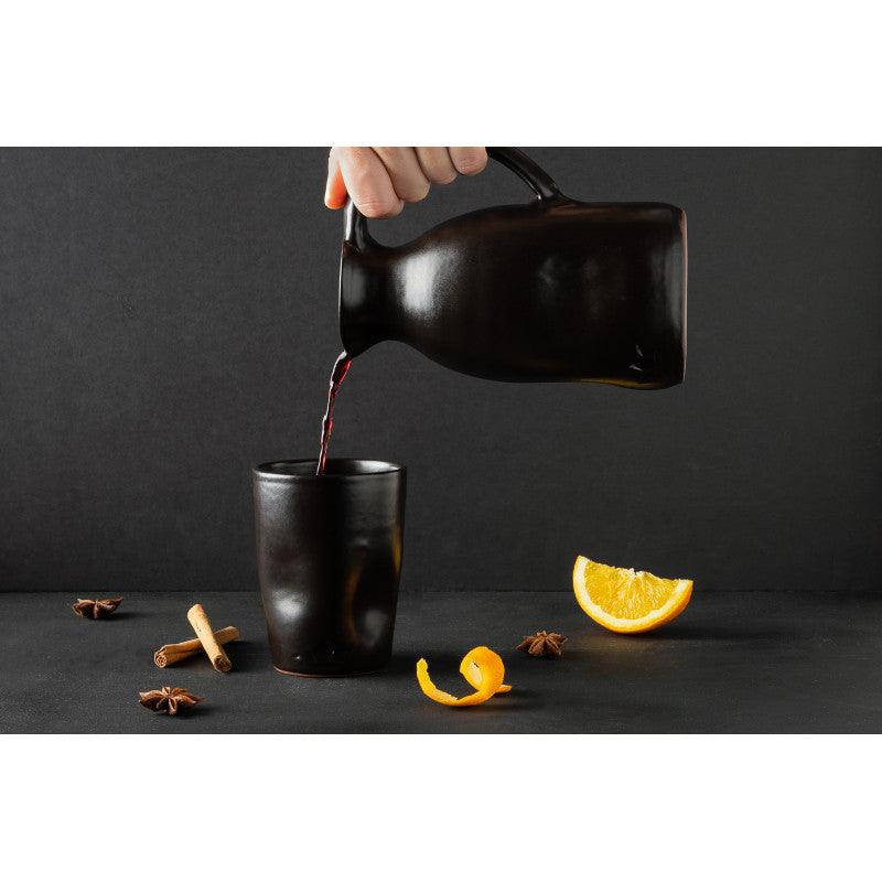 Mano che versa tisana da una caraffa nera in ceramica smaltata Dutch Deluxes, eleganza artigianale in un gesto quotidiano