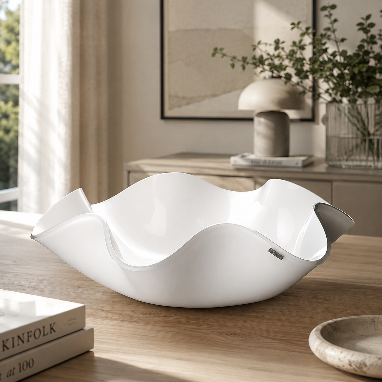 Centrotavola bianco dal design ondulato appoggiato su un tavolo in legno chiaro in un elegante soggiorno moderno. Sullo sfondo dettagli d’arredo minimal nei toni neutri, luce naturale e atmosfera raffinata e contemporanea.