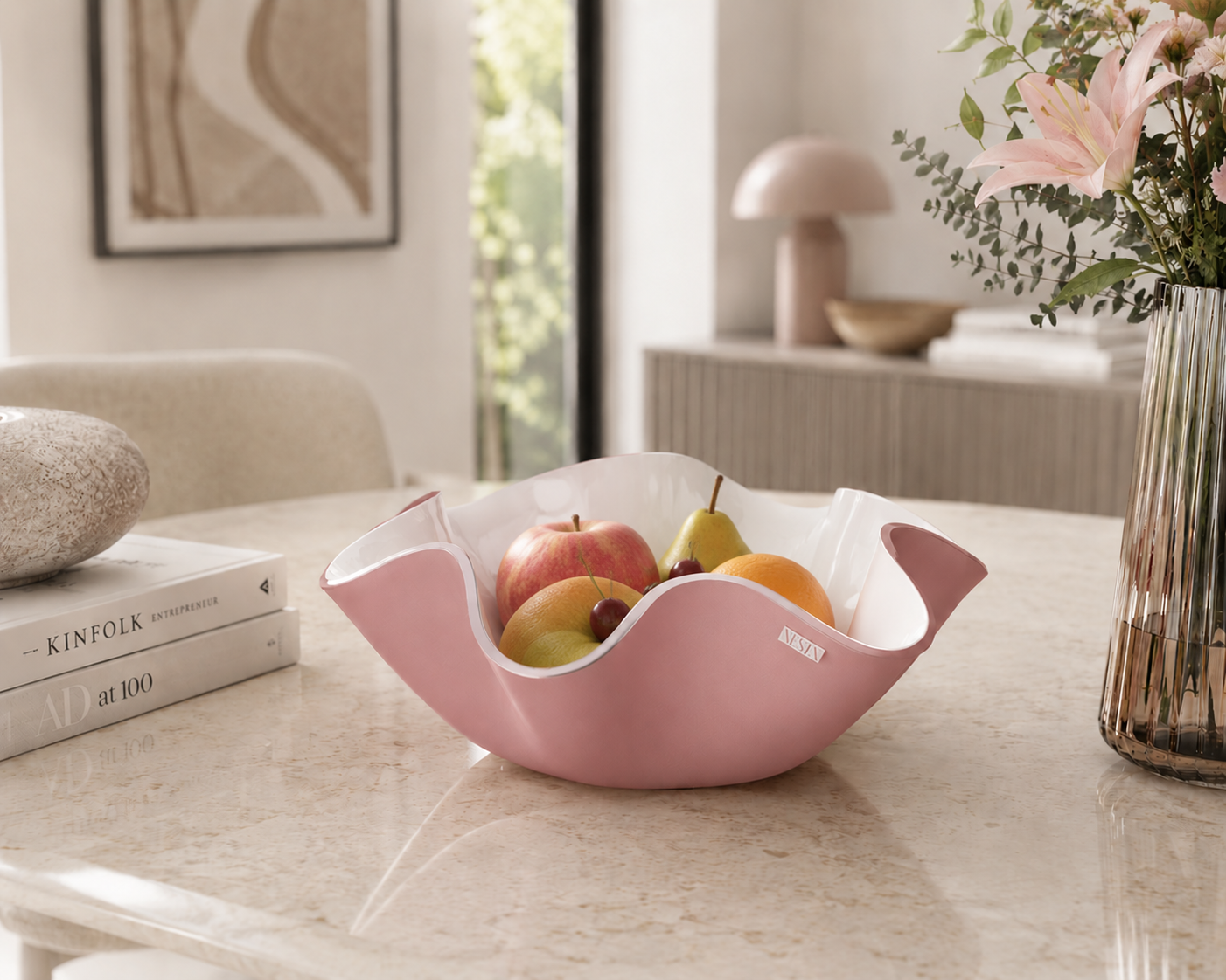 Centrotavola Soft rosa cipria di Vesta Design in cristallo acrilico PMMA con bordo ondulato, ambientato su un elegante tavolo effetto marmo con frutta fresca in un raffinato interno moderno dai toni neutri e luminosi.