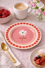 Piatto in porcellana rosa Ø16 cm con fiore bianco e scritta “Cip cip”, ambientato su tavola elegante con caffè, lamponi e dessert
