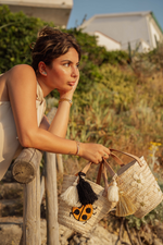 Ragazza che tiene due mini borse in paglia con ricami limone giallo e coccinella rossa davanti al mare al tramonto