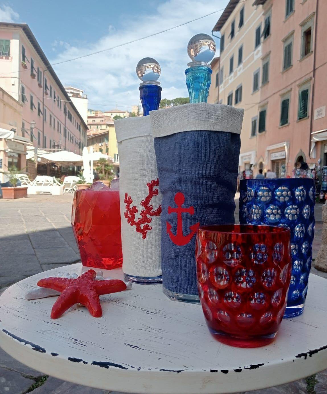copri bottiglia artigianali in lino cerato con ricami nautici e bicchieri colorati Mario Luca Giusti in un allestimento da tavola estiva

