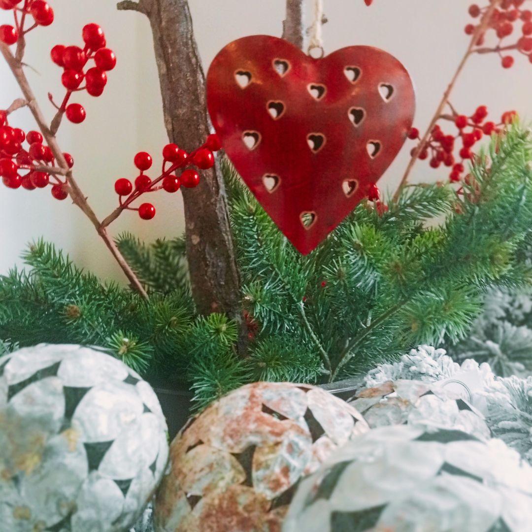 Decorazione natalizia cuore di latta rosso intagliato tra rami verdi e bacche rosse
