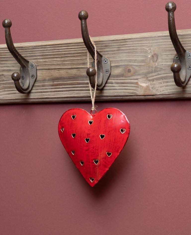 Cuore di latta rosso intagliato appeso a gancio in ferro battuto su parete rustica