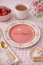 Piatto in porcellana rosa Ø16 cm con scritta “Cuore leggero”, fiori e farfalla, ambientato su tavola con tè e dessert