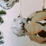 Sfera in ferro con foglie a forma di alloro in primo piano e, sullo sfondo, seconda sfera con foglie in ferro a forma di castagno. Oggetti décor artigianali.