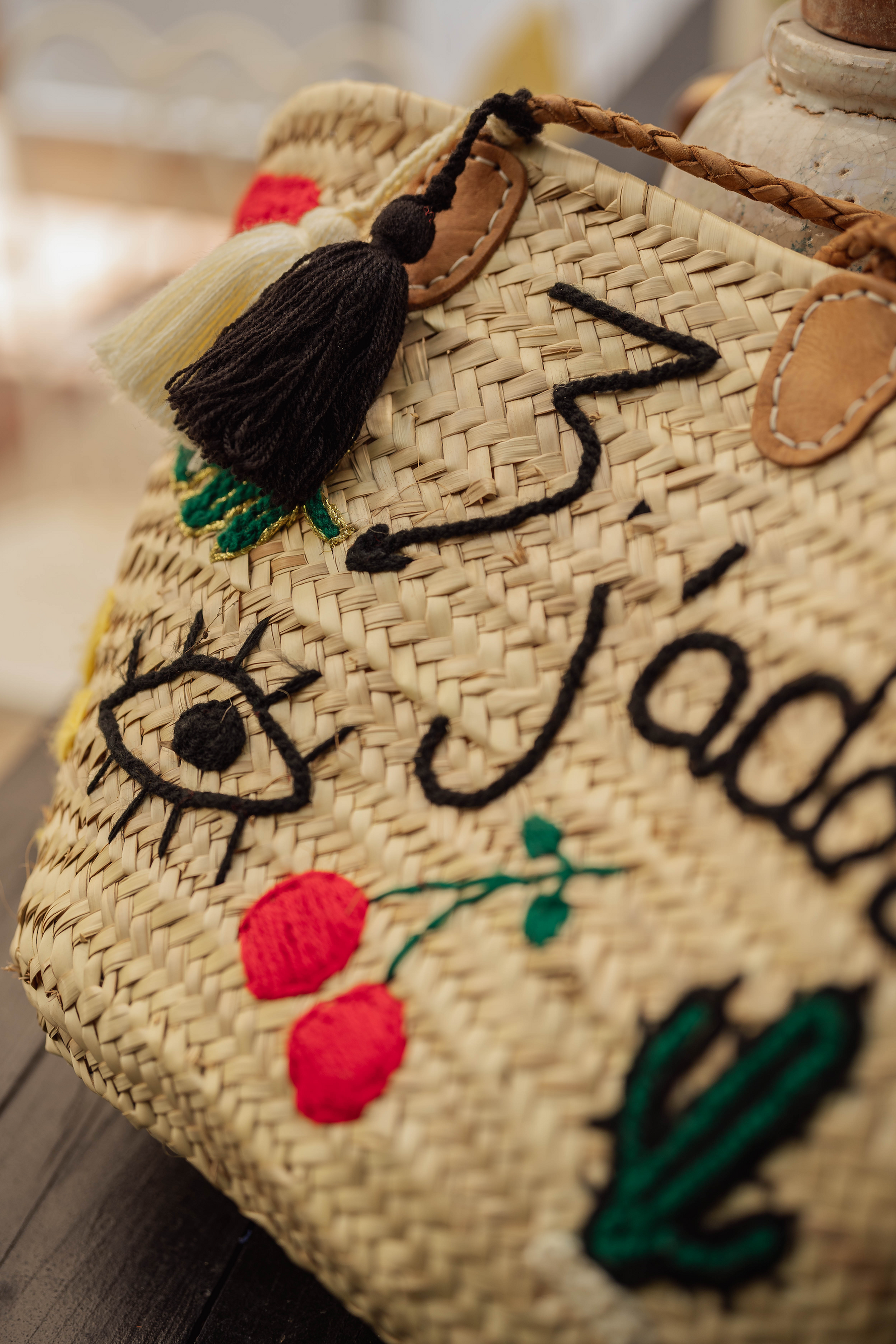 Dettaglio borsa J’Adore in paglia con ricamo scritta, ciliegie rosse, cactus verde e occhio portafortuna.