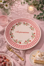 Piatto in porcellana “È la primavera” Ø21 cm con decoro floreale rosso e verde e bordo rosa, apparecchiato su tavola rosa con dolci, candela e fiori in stile romantic