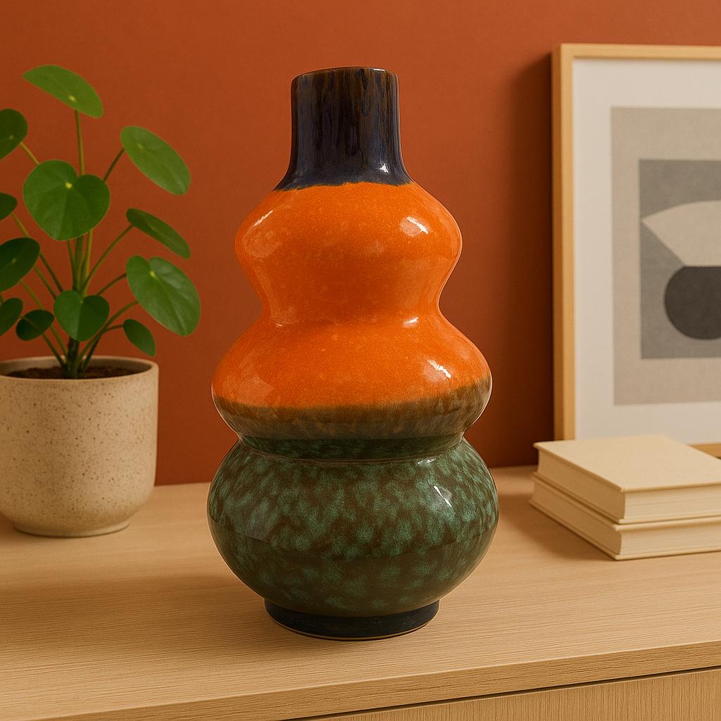 Vaso decorativo in ceramica con doppia bombatura, smaltato in arancione, verde e nero, appoggiato su una mensola in un ambiente modern