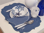 Mise en place estiva con americano e tovagliolo in lino cerato blu, ricami marini bianchi e piatti decorati con coralli, ideale per tavole eleganti al mare