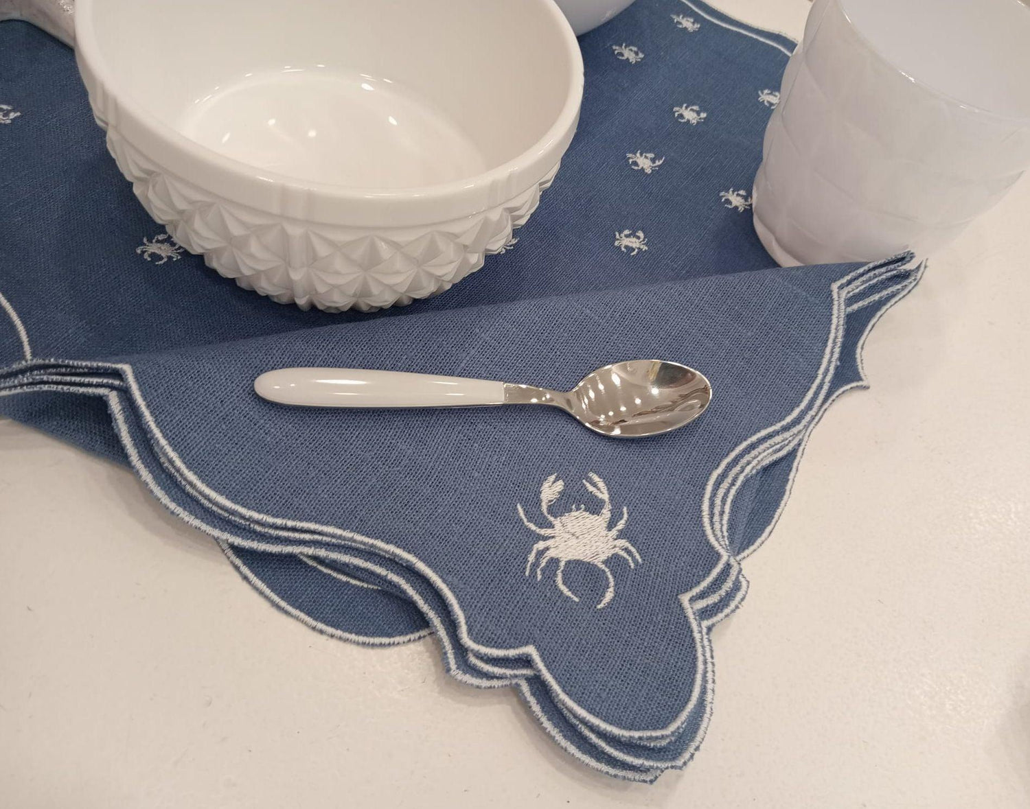 Dettaglio tovaglietta americana blu con ricamo a granchio bianco e accessori per la tavola