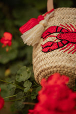 Borsa cestino in paglia intrecciata con ricamo aragosta rossa e nappine decorative, accessorio artigianale estivo