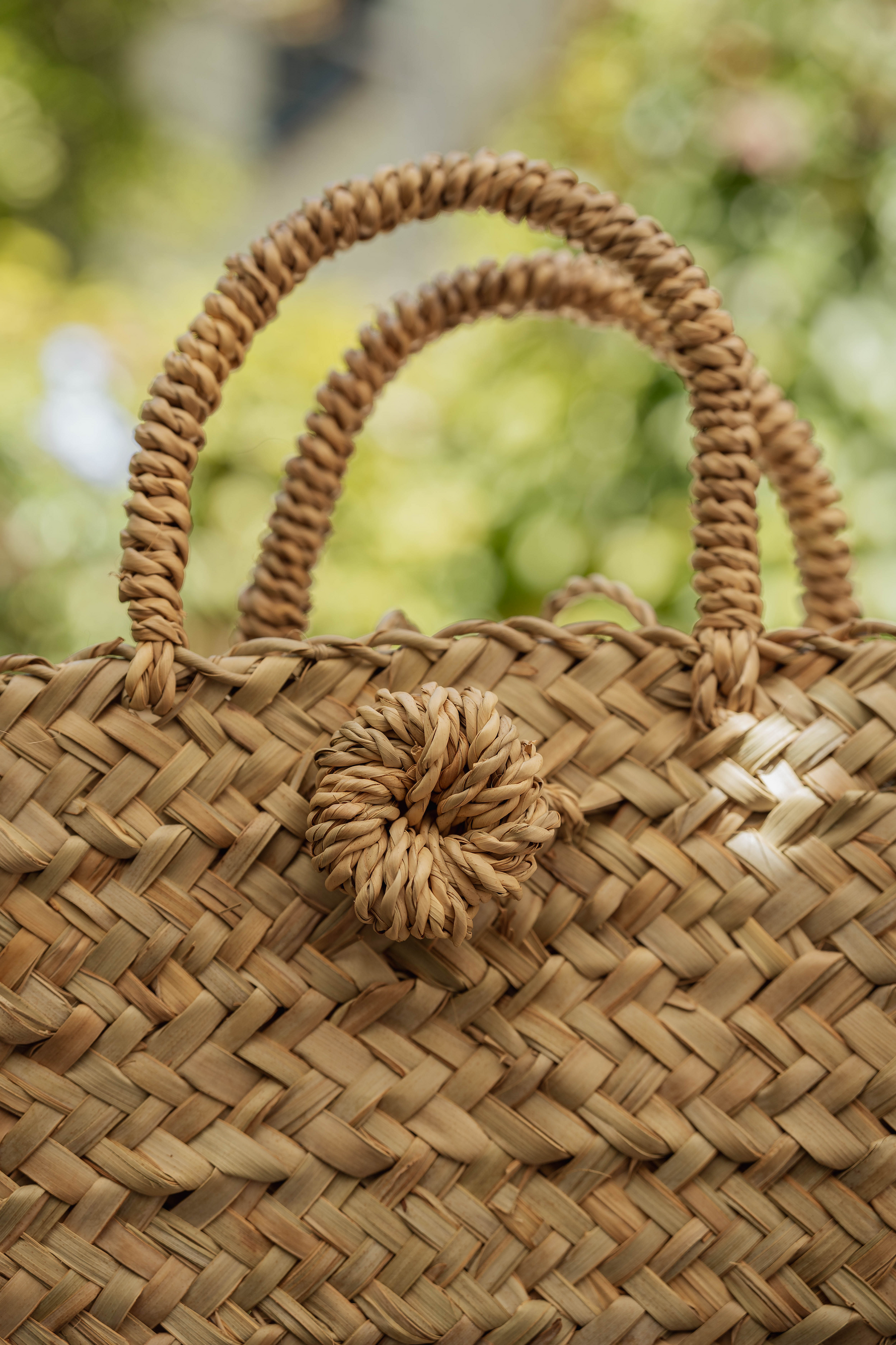 Dettaglio borsa artigianale in paglia intrecciata con manici e chiusura a spilla in fibra naturale, stile estivo boho chic