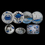 Servizio tavola in melamina Oceano Illustrato con piatti piani, dessert, fondi e vassoi decorati con illustrazioni marine blu e nere

