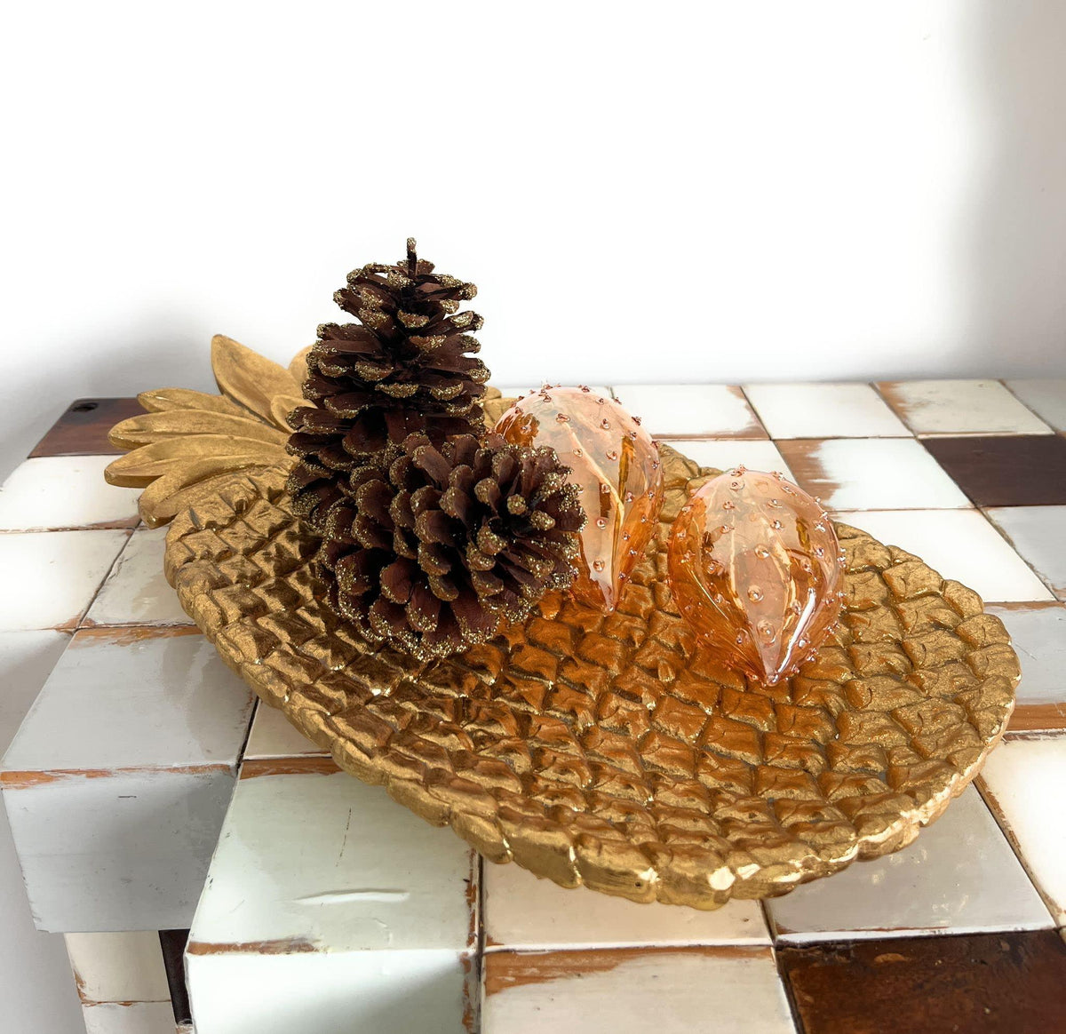 Dettaglio vassoio dorato a forma di ananas EDG con pigne glitterate e decorazioni in vetro ambrato, ambientazione elegante e festiva.