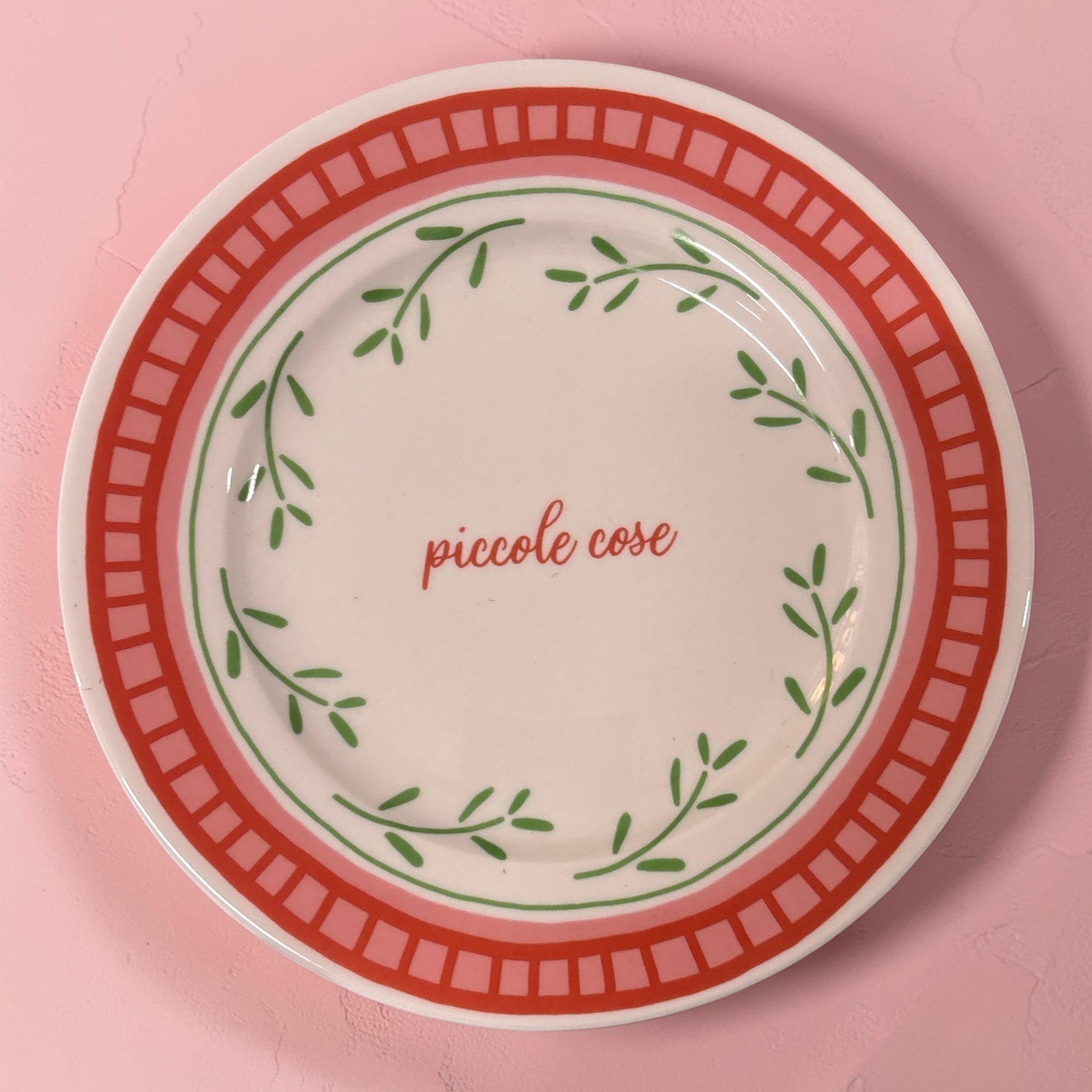 Piatto in porcellana Ø21 cm con scritta “piccole cose”, decoro foglie verdi e bordo rosso pesca su fondo rosa