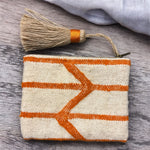 Pochette artigianale Marika Selection in tessuto berbero beige con motivi geometrici arancio e nappina laterale, accessorio boho etnico