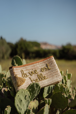Pochette in paglia intrecciata con scritta La vie est belle ricamata appoggiata su cactus, Marika Selection