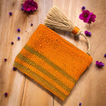 Pochette artigianale in tessuto berbero arancione con righe verde salvia con pappina fotografata su legno con fiori viola