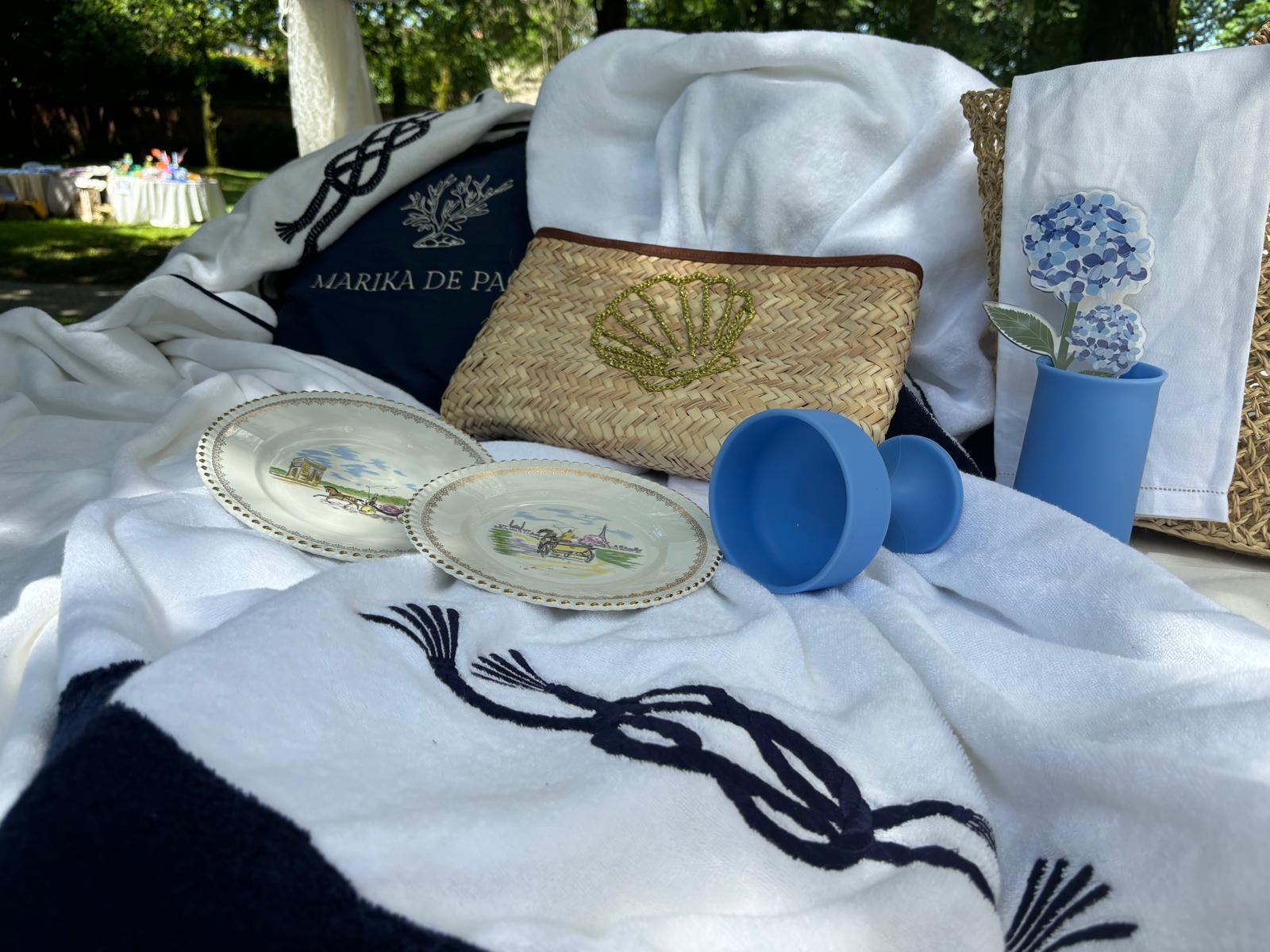 teli mare bianchi con bordo e ricamo nodo marino blu, artigianali made in Italy, esposti con accessori estivi e piatti decorativi su letto outdoor