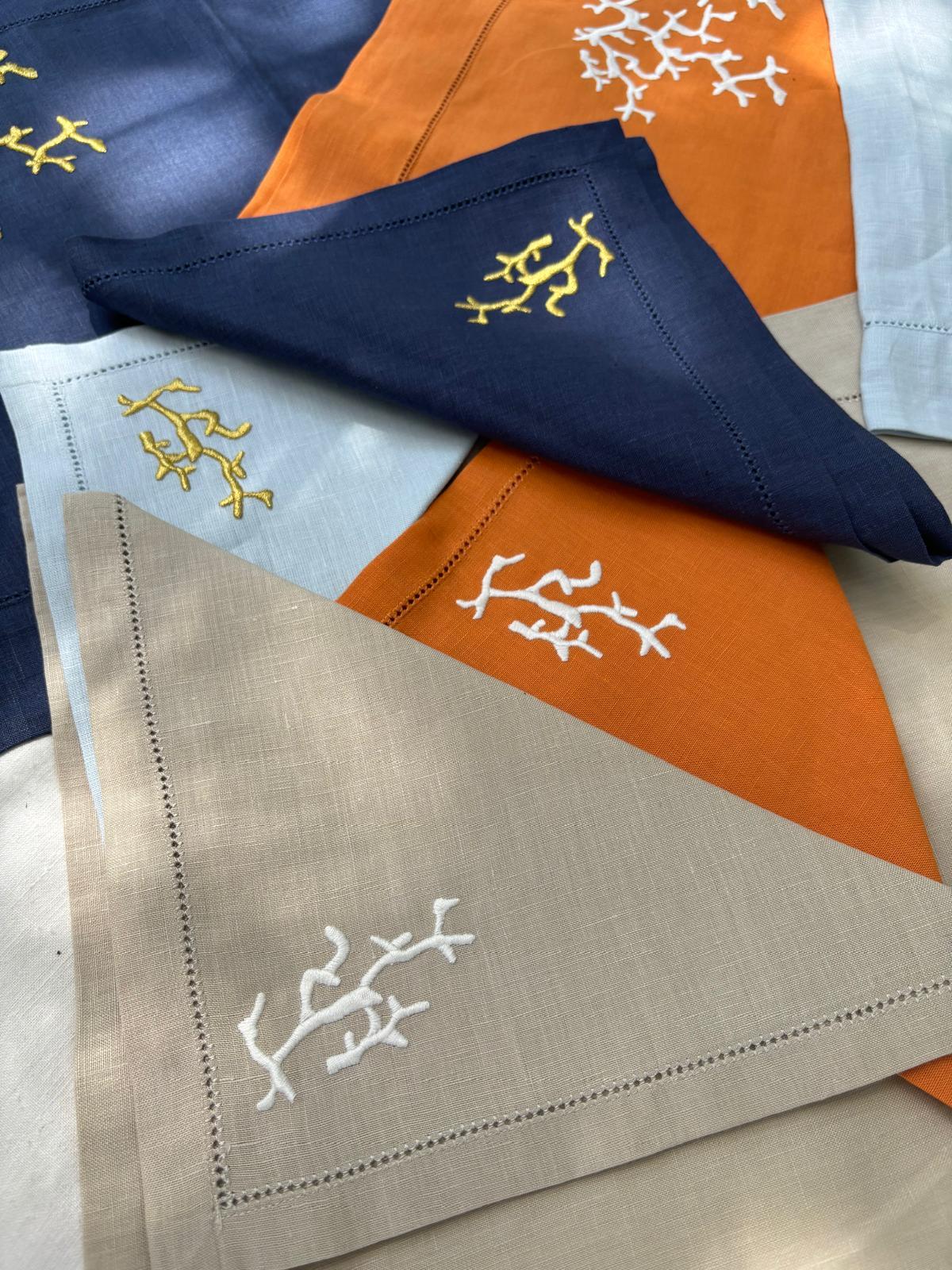 Tovaglioli ricamati a mano con corallo, nei colori arancio, blu, azzurro e beige e particolari di americano arancio e blu