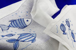 Americano e tovagliolo in lino bianco con pesci blu ricamati a mano – artigianato italiano di lusso a tema marino