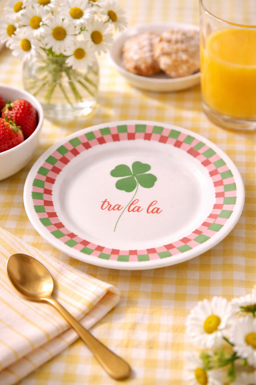 Piatto in porcellana bianco Ø16 cm con quadrifoglio verde e scritta “Tra la la”, ambientato su tavola primaverile con fragole e succo d’arancia