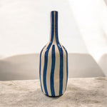 Vaso in ceramica bianco e azzurro con righe verticali dipinte a mano, fotografato su sfondo luminoso.”