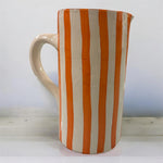 Vaso artigianale in ceramica a righe arancio e terracotta con un manico, fatto a mano, stile mediterraneo, ambientato su tavolo in legno