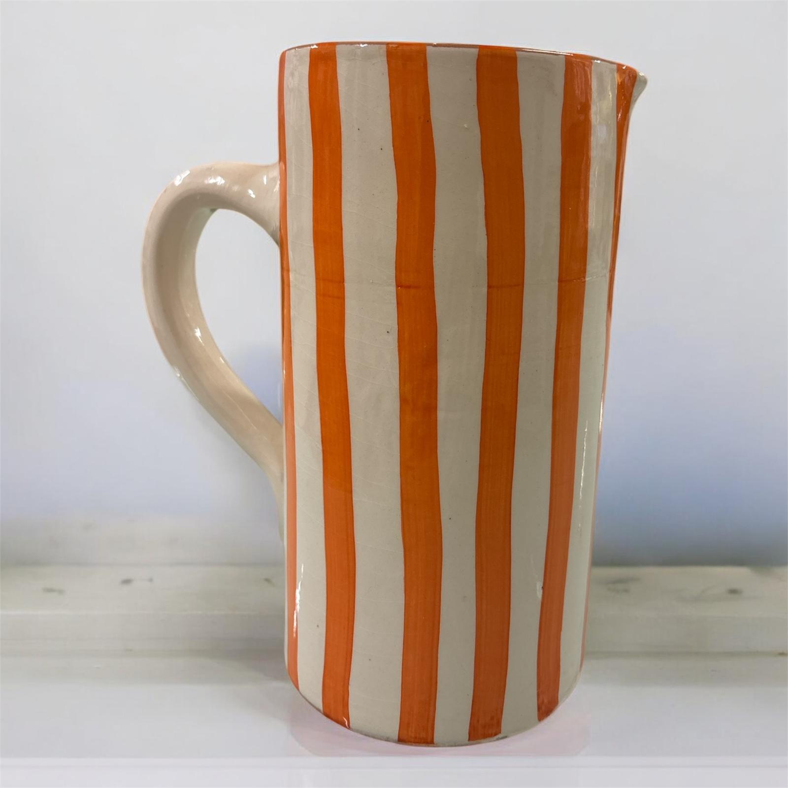 Vaso artigianale in ceramica a righe arancio e terracotta con un manico, fatto a mano, stile mediterraneo, ambientato su tavolo in legno