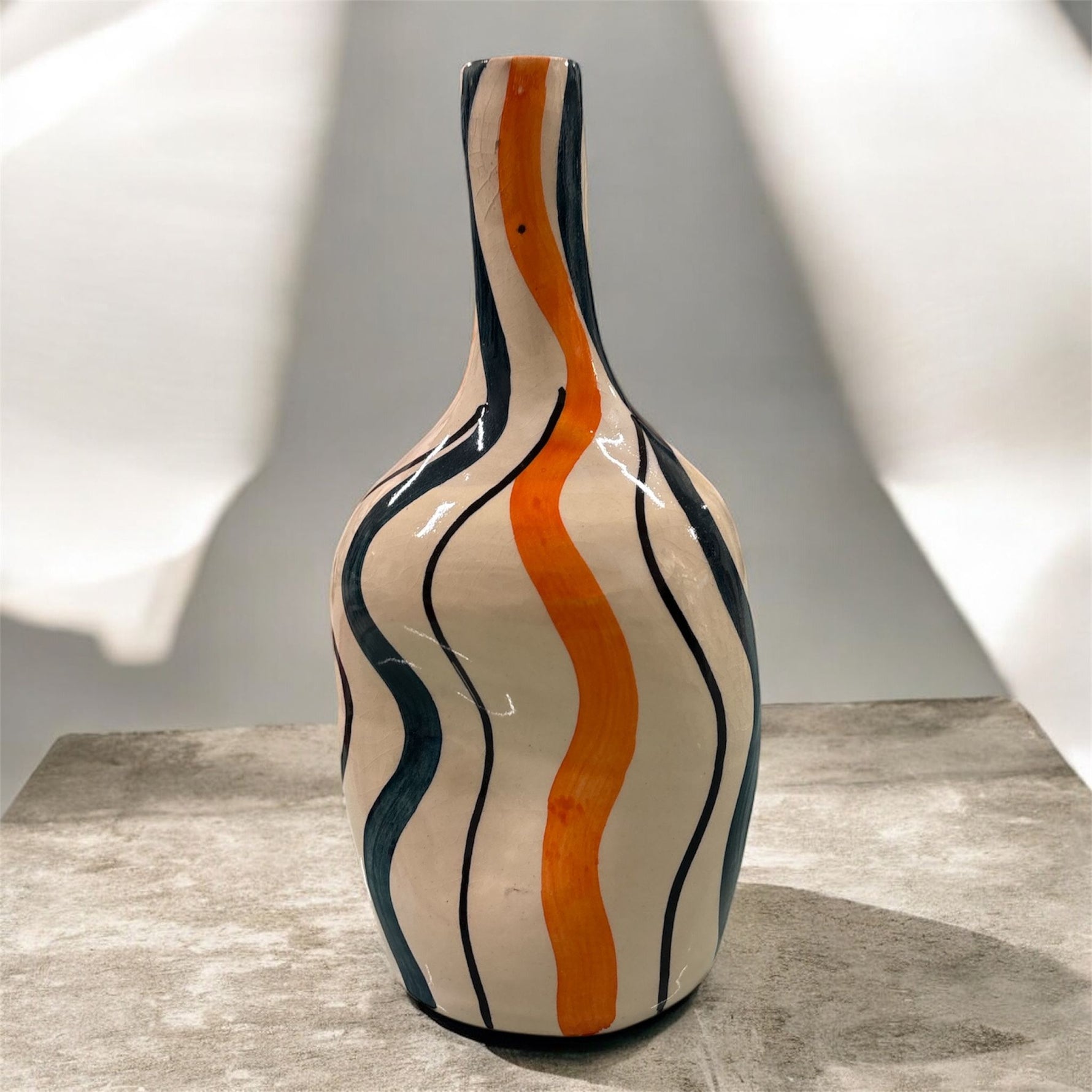 Vaso artigianale con onde arancioni e verde-blu esposto su superficie neutra in ambiente luminoso.