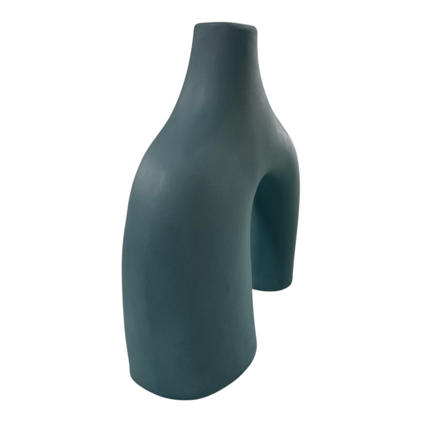 Vaso azzurro opaco in ceramica visto lateralmente, design scultoreo a due piedi.