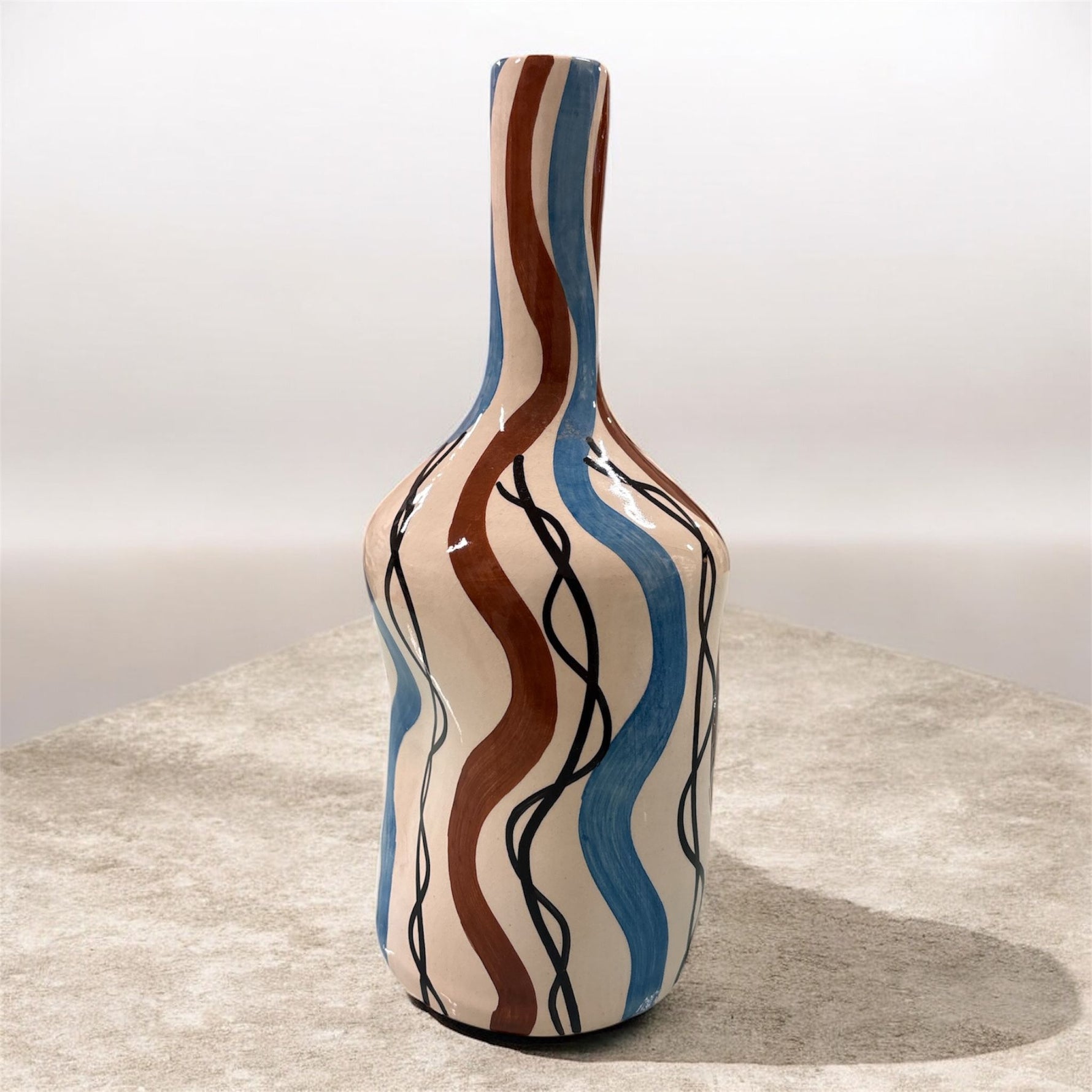 Vaso artigianale con onde marroni e azzurre in un ambiente luminoso.