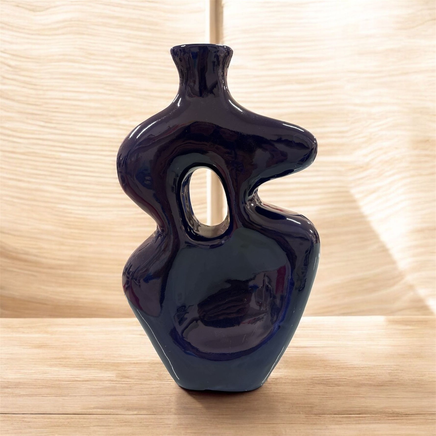 Vaso scultoreo in ceramica blu notte con apertura centrale, posato su piano in legno in ambiente luminoso