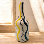 Vaso artigianale in ceramica con onde gialle e verdi vicino a una finestra.