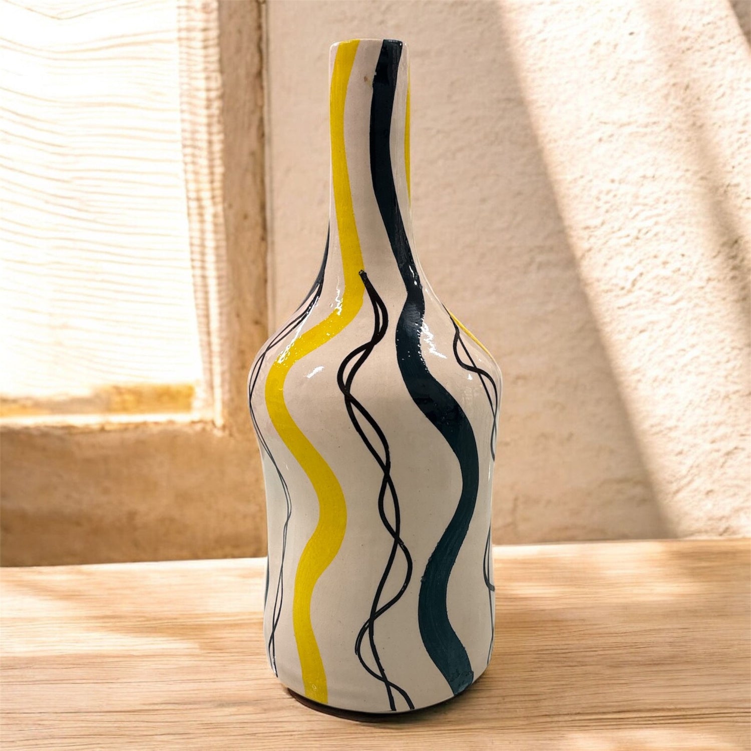 Vaso artigianale in ceramica con onde gialle e verdi vicino a una finestra.