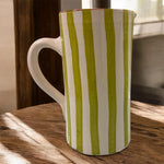 Vaso artigianale in ceramica a righe verde e terracotta con un manico, fatto a mano, stile naturale, ambientato in interno luminoso