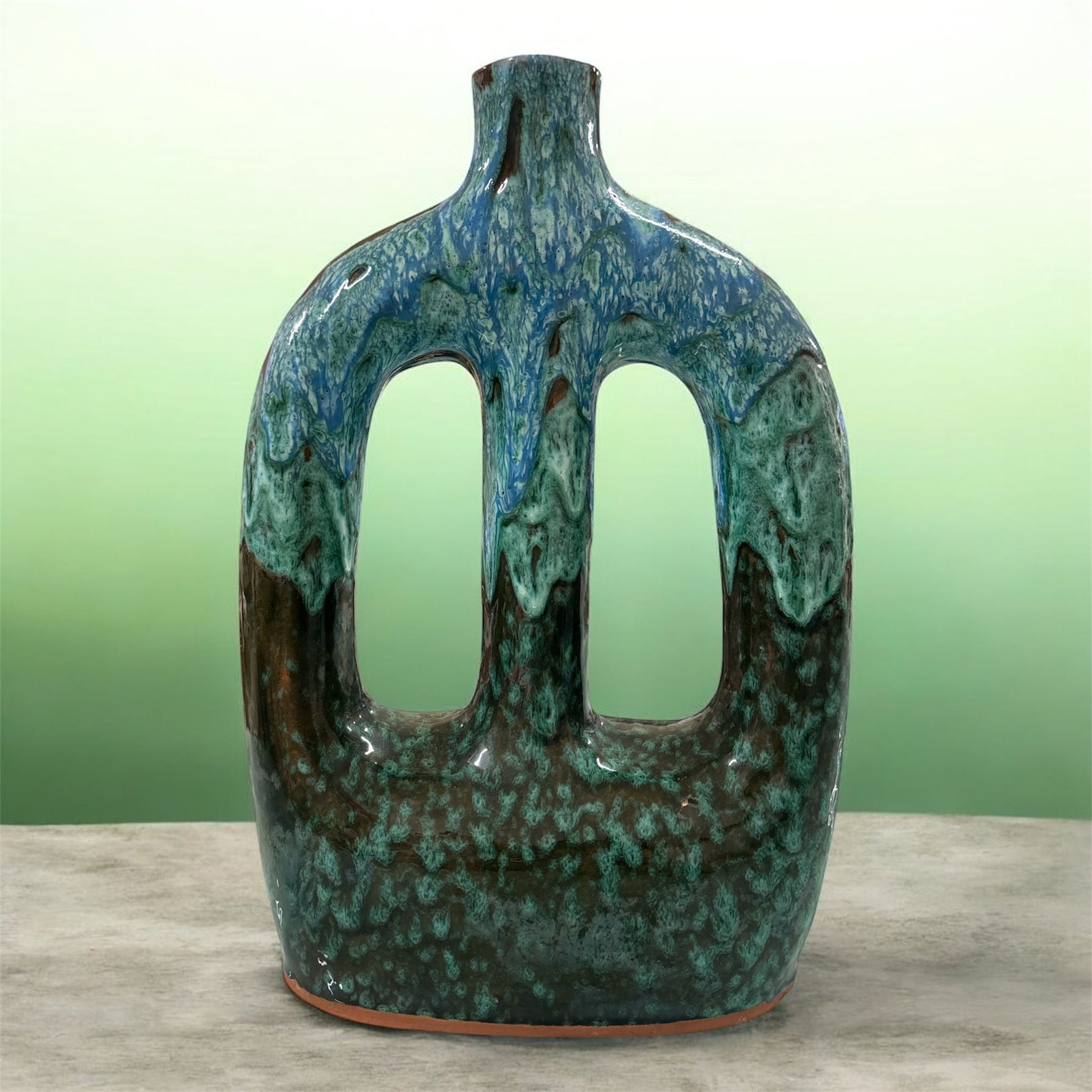 Vaso in ceramica verde e blu a doppio manico su superficie neutra e sfondo verde sfumato