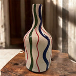 Vaso artigianale con onde blu, verdi e rosse fotografato in ambiente naturale con luce calda