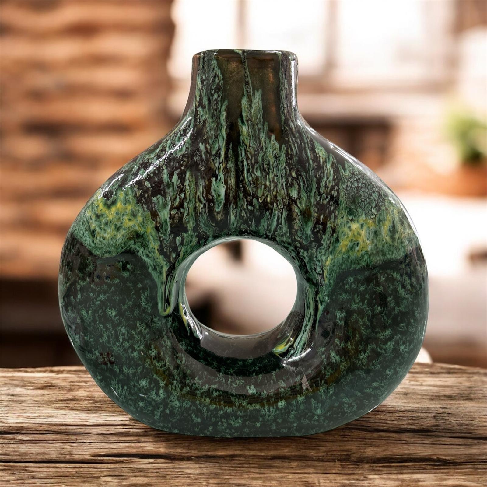 Vaso decorativo in ceramica verde con forma moderna a ciambella e finitura marmorizzata, appoggiato su un tavolo in legno