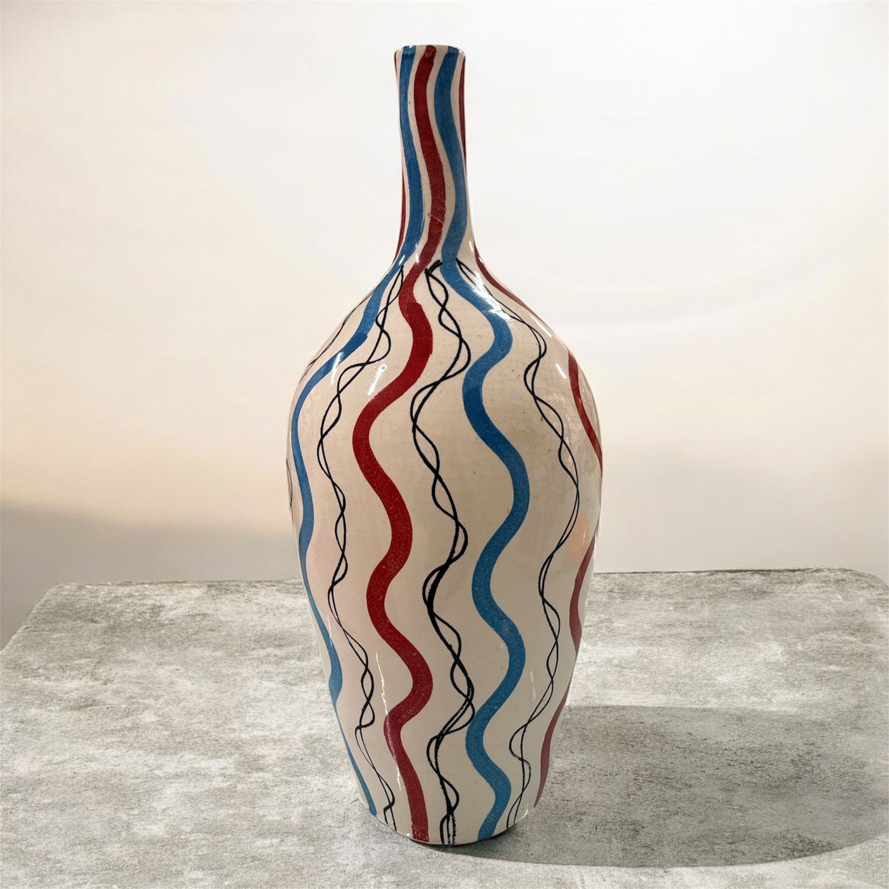 Vaso in ceramica alto 42 cm con onde rosse, blu e nere dipinte a mano, fotografato su superficie chiara.