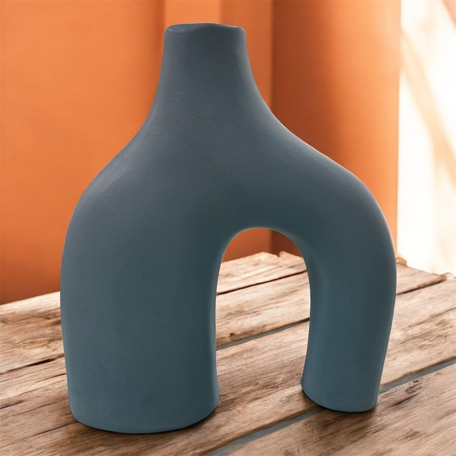 Vaso artigianale azzurro opaco in ceramica con doppio piede, ambientato su superficie in legno.