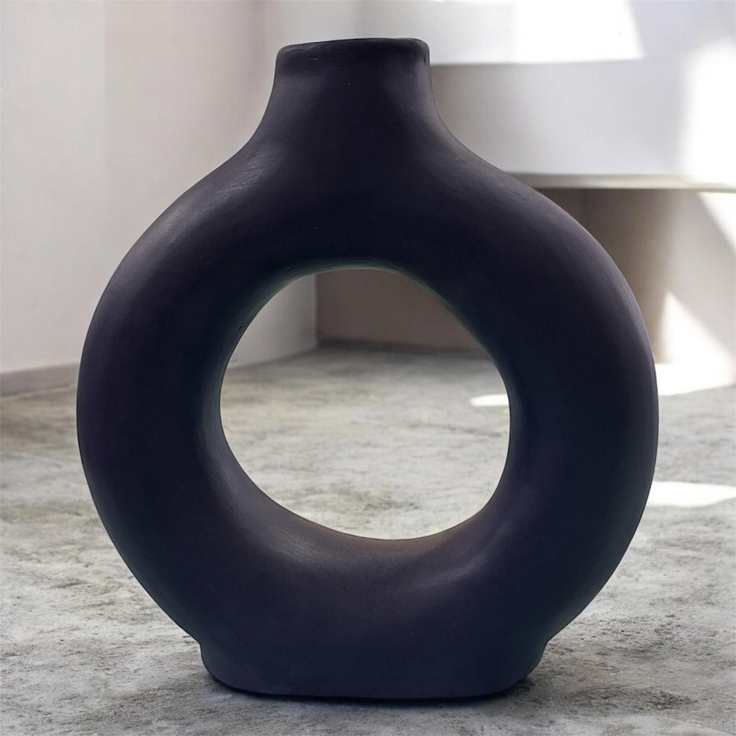 Vaso artigianale blu notte in ceramica con foro centrale, ambientato in un interno moderno.