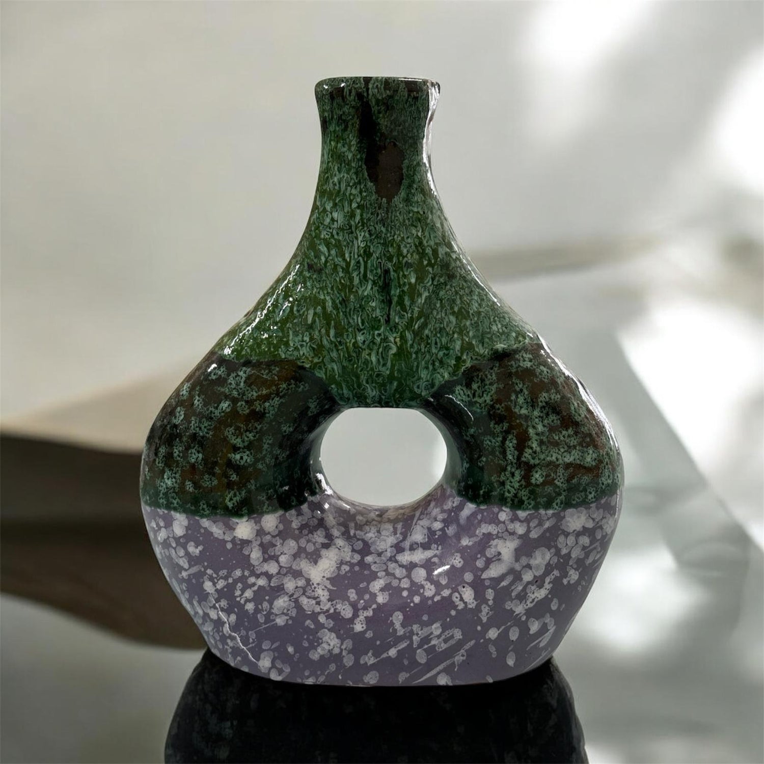 Vaso Bicolore in ceramica verde e viola con foro centrale, fotografato su superficie riflettente.